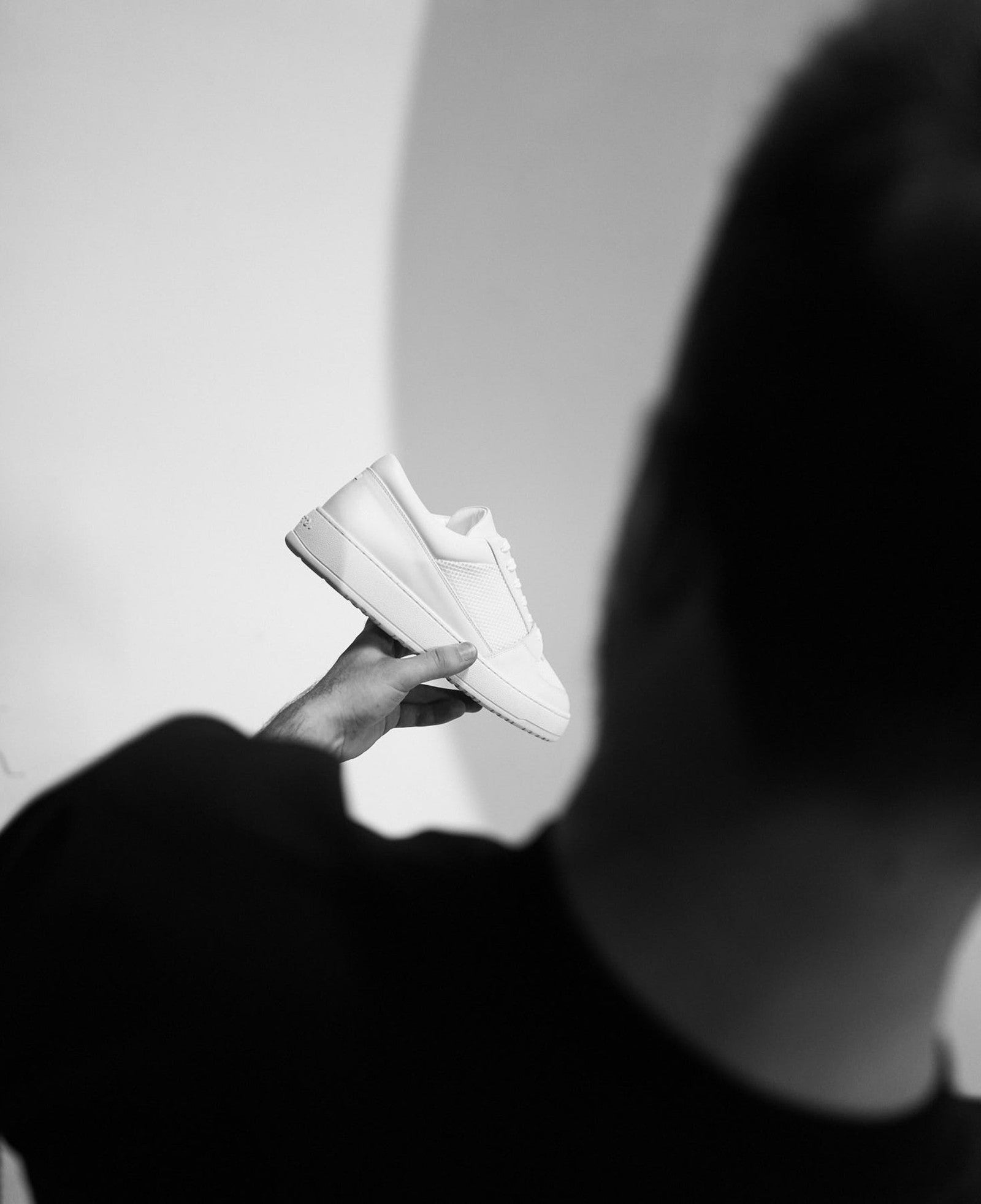 A finished white ETQ sneaker held in hand